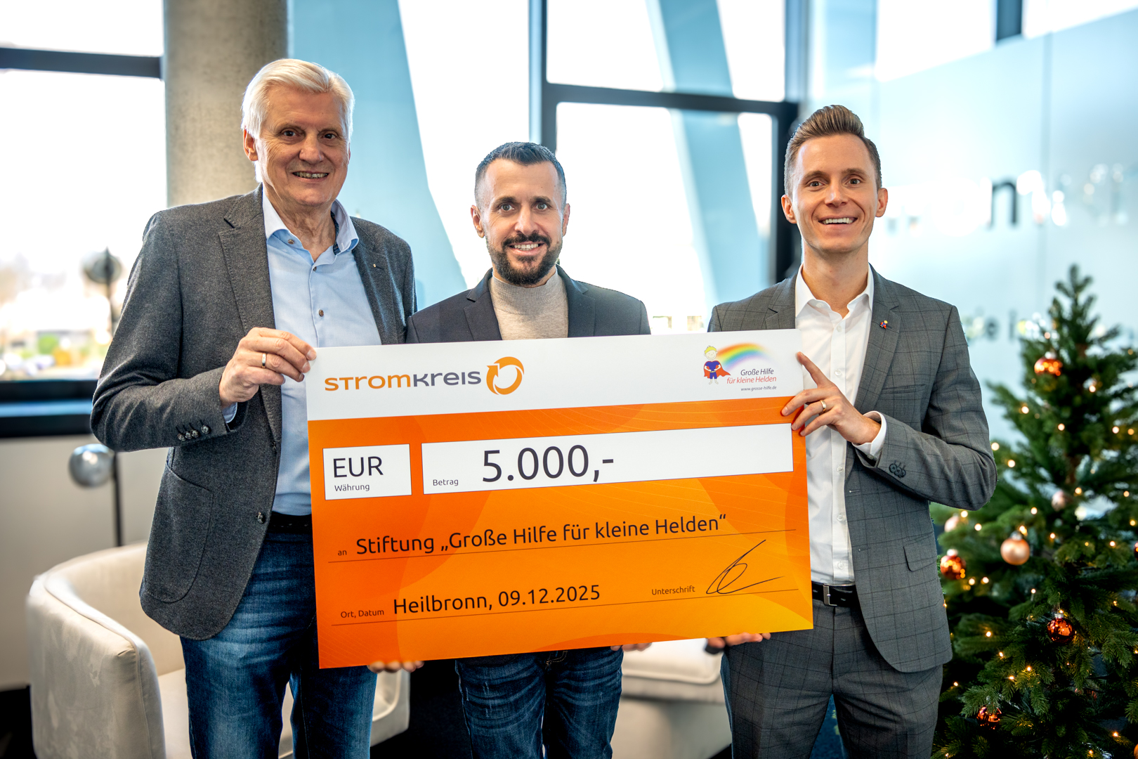 GHFKH_Scheckuebergabe_2025 3 Männer halten einen Spendencheck in der Hand vor einem Weihnachtsbaum